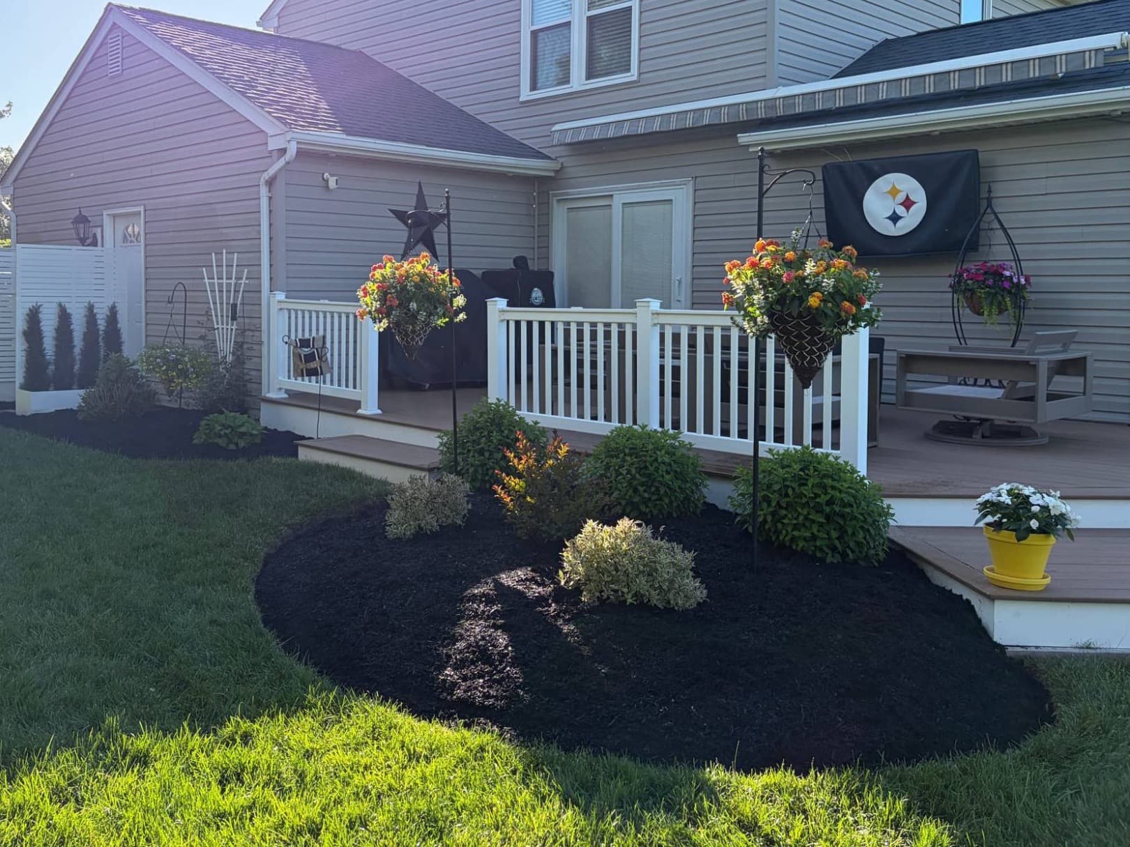 Backyard bed beside a deck, cleaned and finished with fresh black mulch around new shrubs