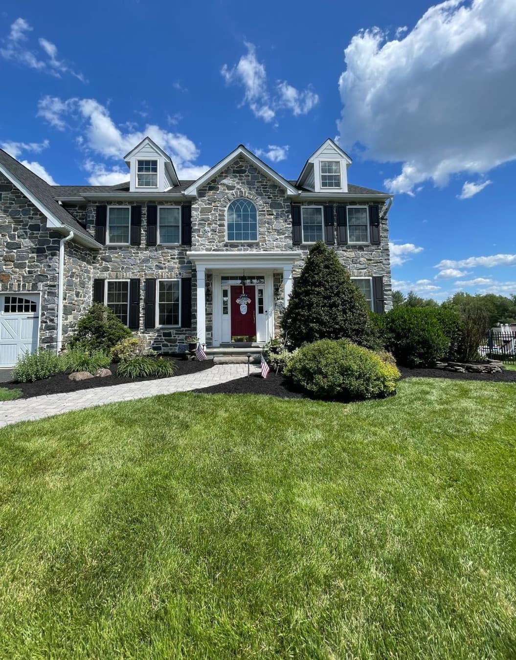 Stone colonial home with neatly shaped shrubs along freshly mulched front beds