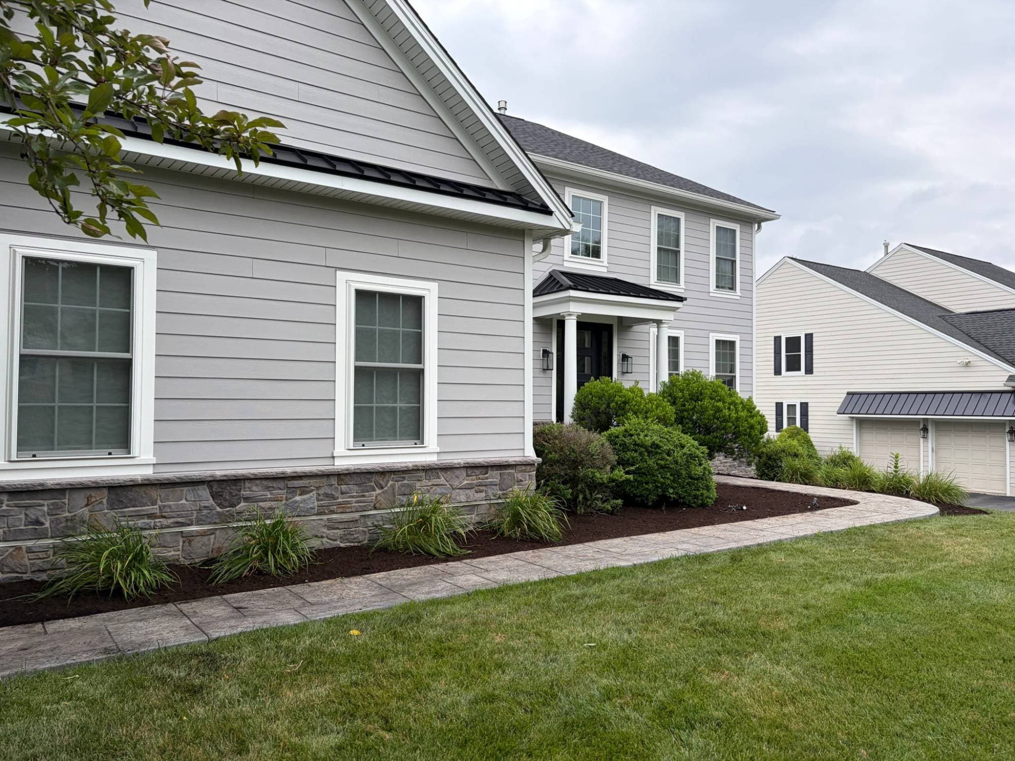 Foundation bed along a stone-trimmed home and curved walkway, freshly mulched around daylilies and shrubs